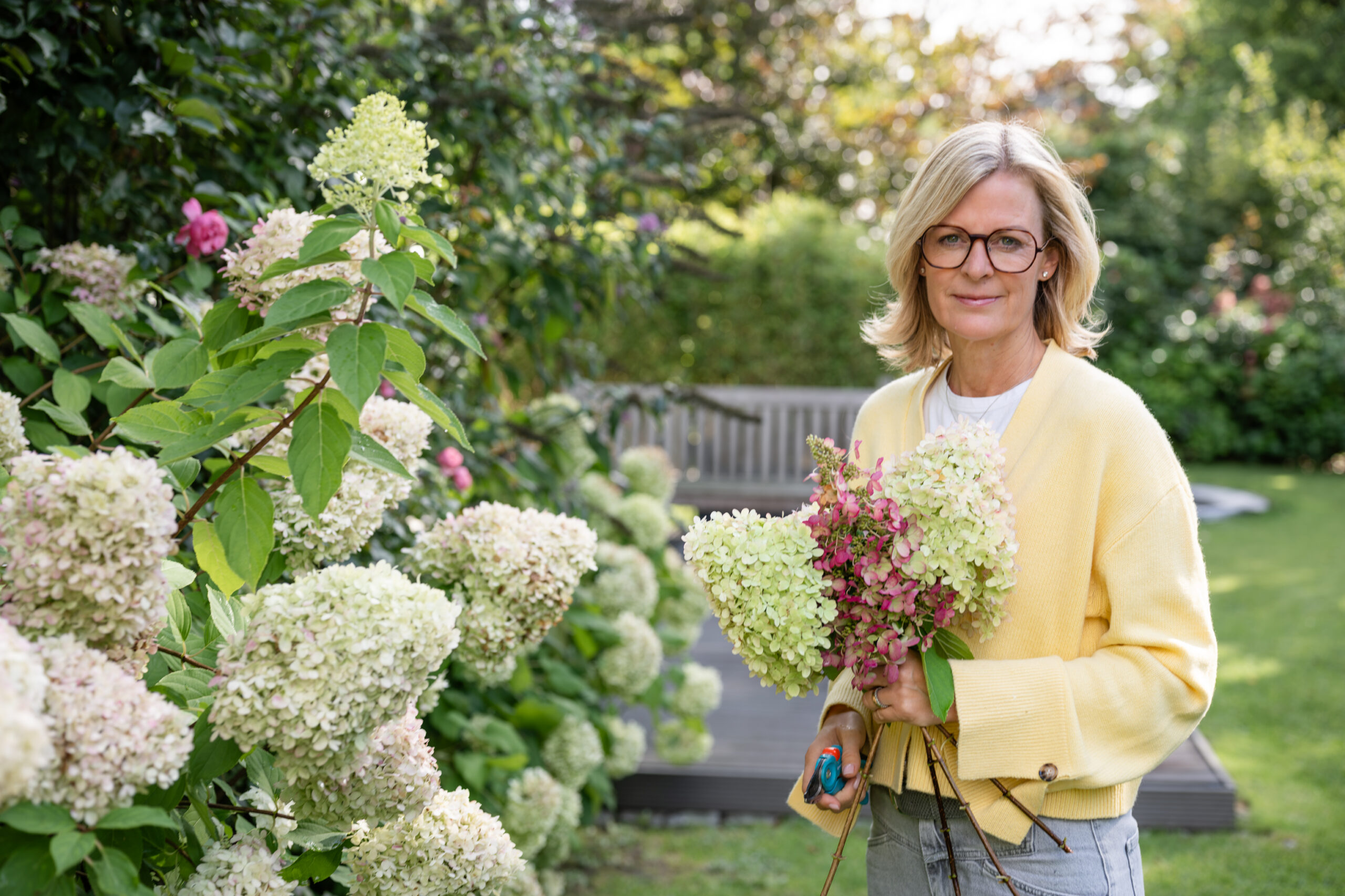 Corinna Starcke steht mit Hortensien im Garten und lächelt
