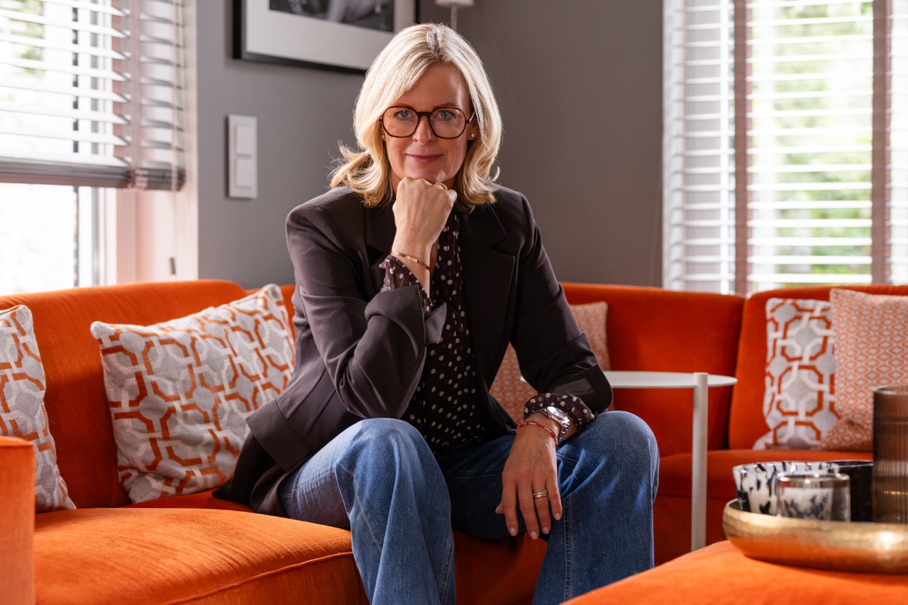 Corinna Starcke nachdenklich auf dem Sofa, Querformat Paarberaterin Corinna Starcke sitzt nachdenklich auf einem orangen Sofa