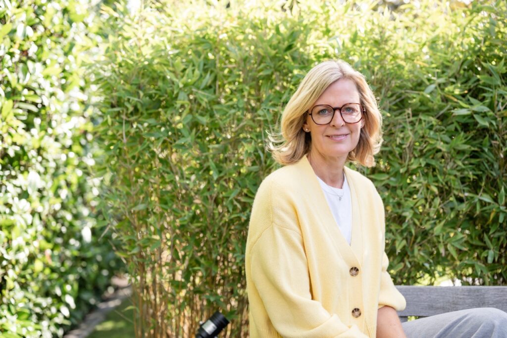 Paarberaterin Corinna Starcke sitzt im Garten auf einer Bank vor einer hohen Hecke
